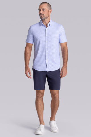 Model wearing Rhythm Santorini Blue 6-Way Knit® short sleeve casual shirt with collar placket, styled with navy shorts.
